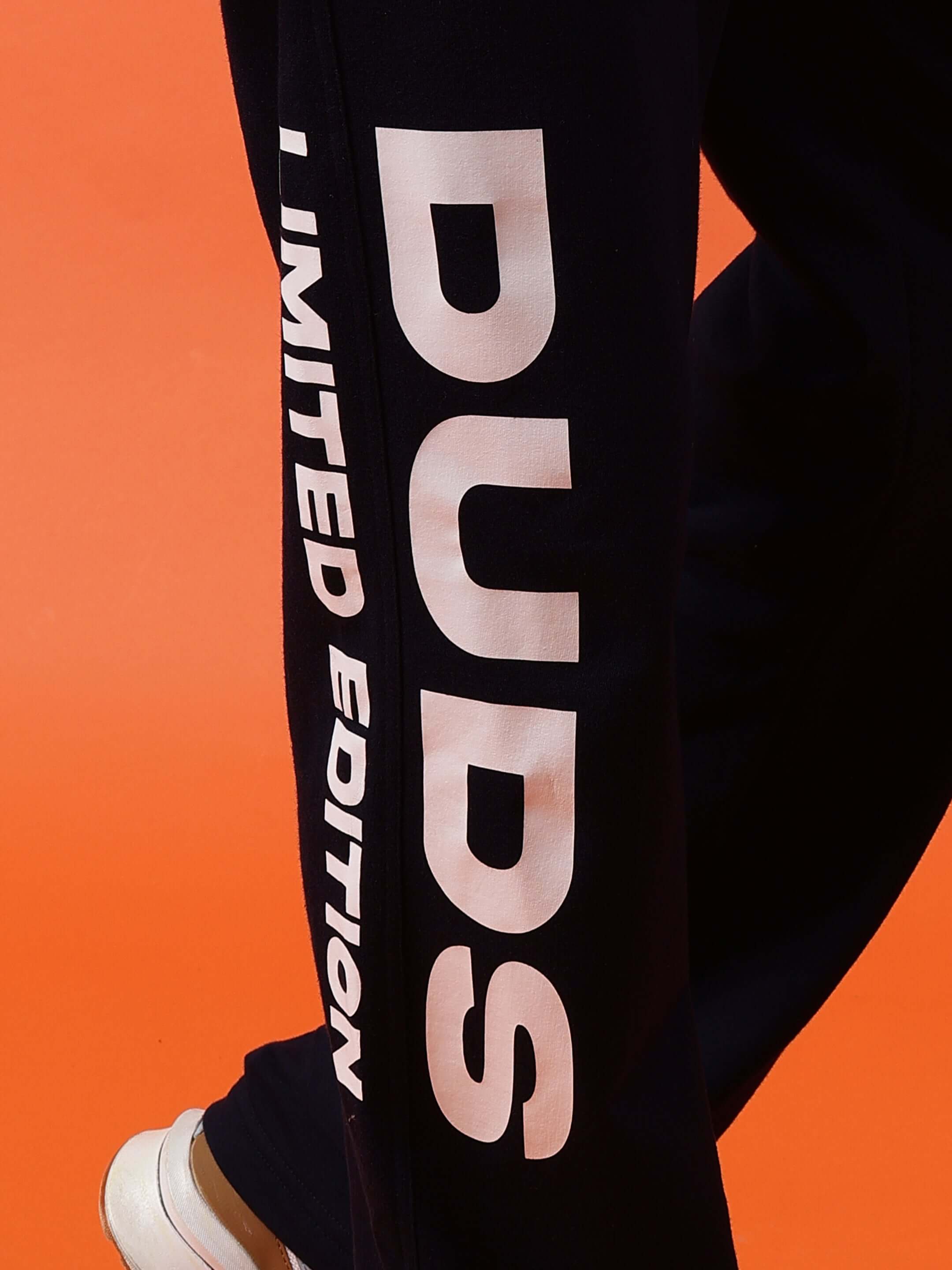 DUDS Limited Edition Navy Blue Jogger with bold white lettering, shown against orange background. Perfect for personalized fit.