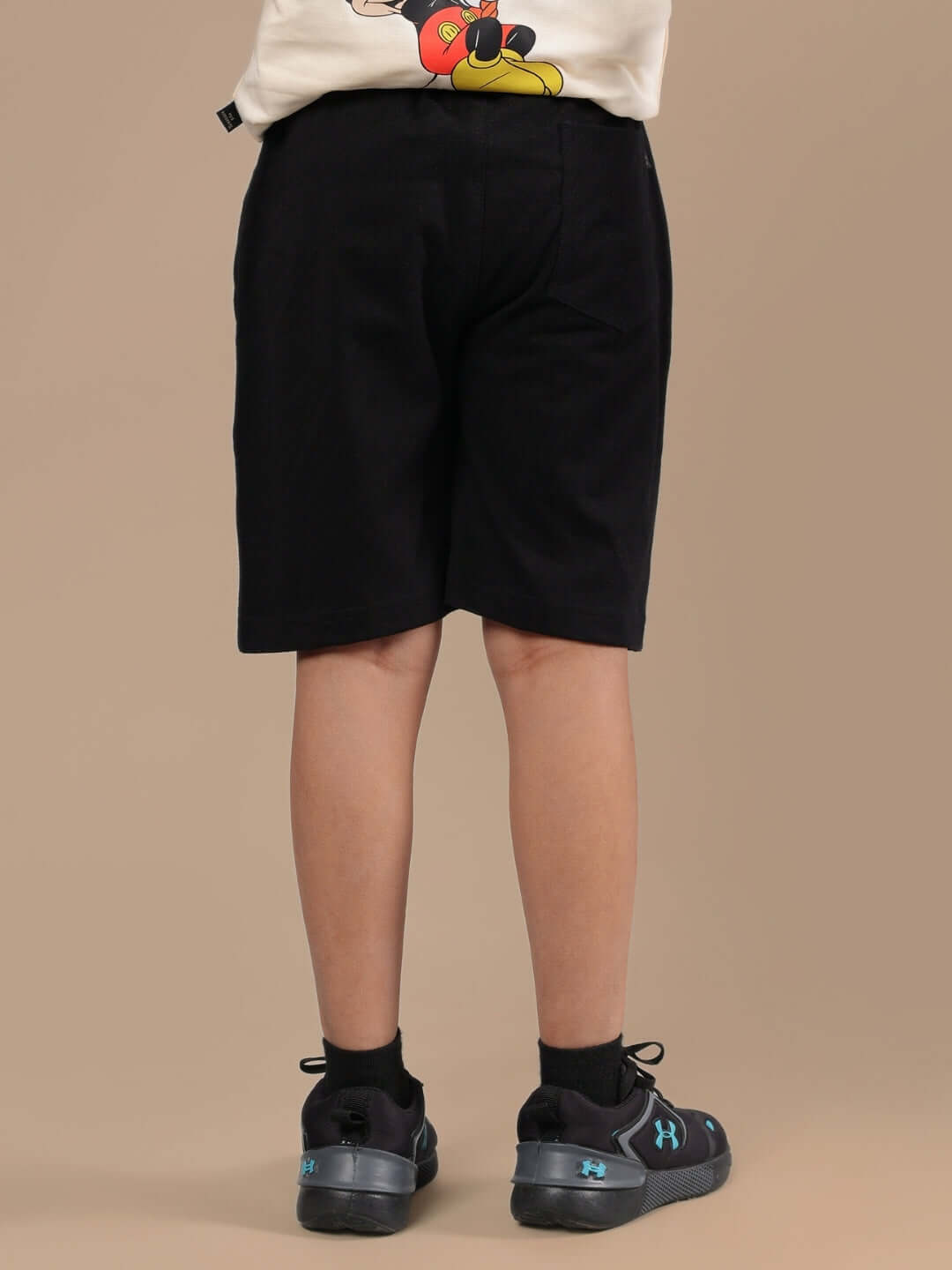 Child wearing DUDS MOUSE SHORTS FOR BOYS & GIRLS BLACK with a cartoon shirt and sneakers, showcasing back view.