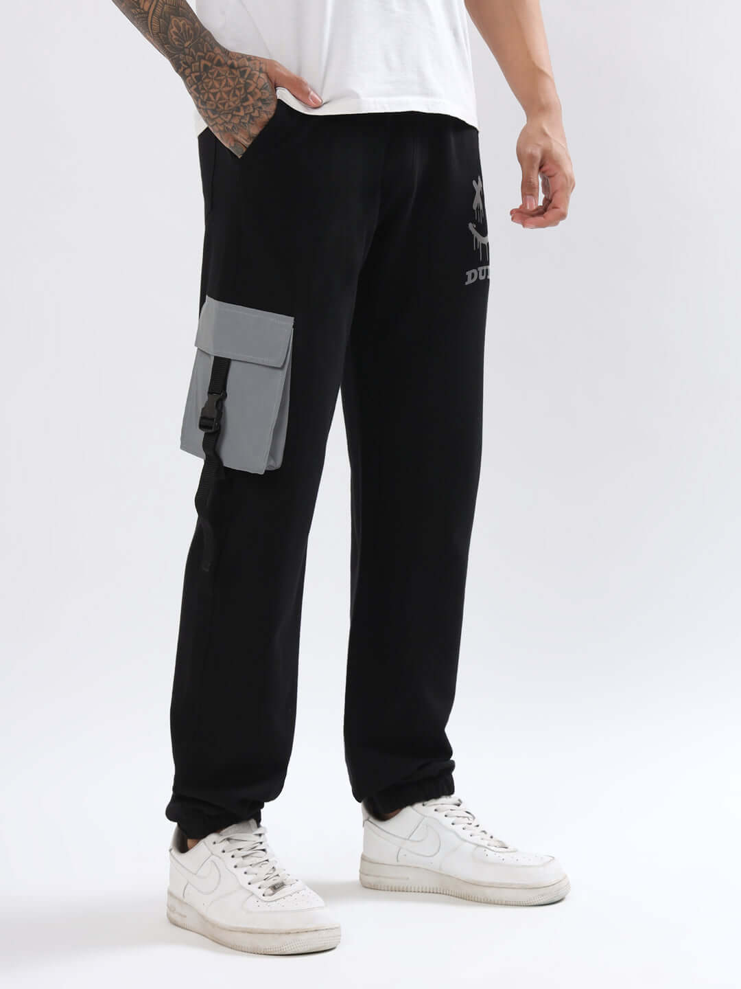 Black cargo jogger pants with smiley reflector design and side pocket, worn by a person wearing white sneakers and a white shirt.