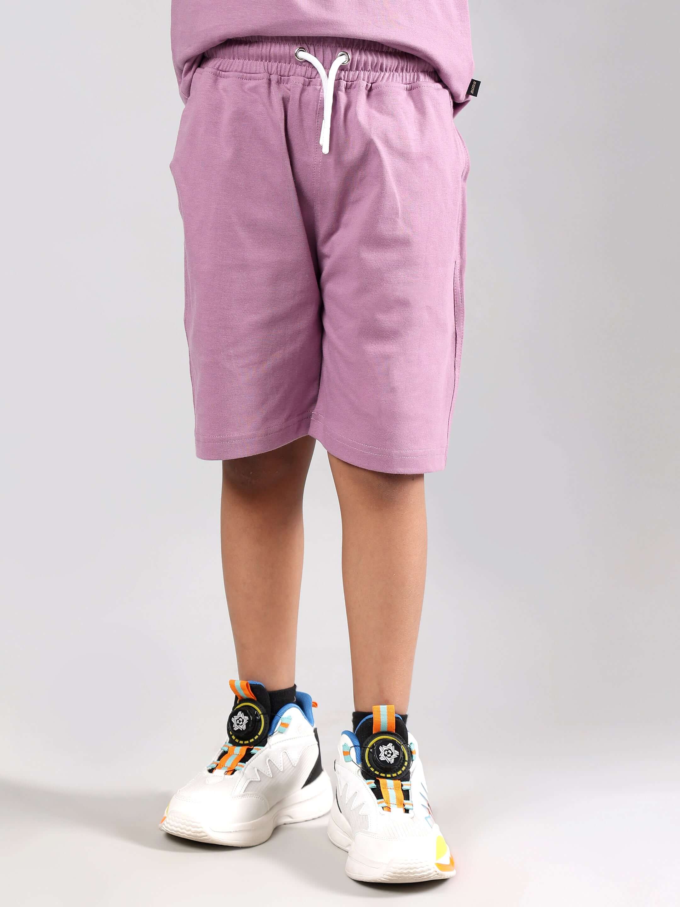Child wearing DUDS Street Co-ord in plum purple, featuring comfortable shorts with a drawstring and white sneakers.