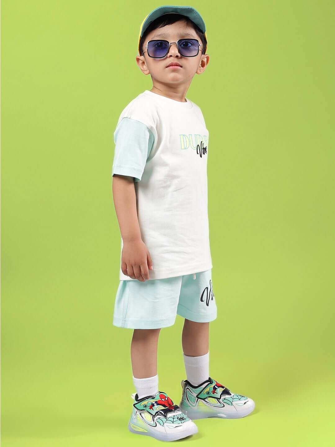 Boy wearing DUDS VIBES CO-ORD FOR BOYS & GIRLS OFF WHITE-BLUE on green background, featuring off-white shirt and blue shorts ensemble.