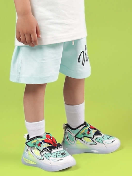 Child wearing DUDS VIBES SHORTS FOR BOYS & GIRLS SKY BLUE with colorful sneakers standing on a green background.
