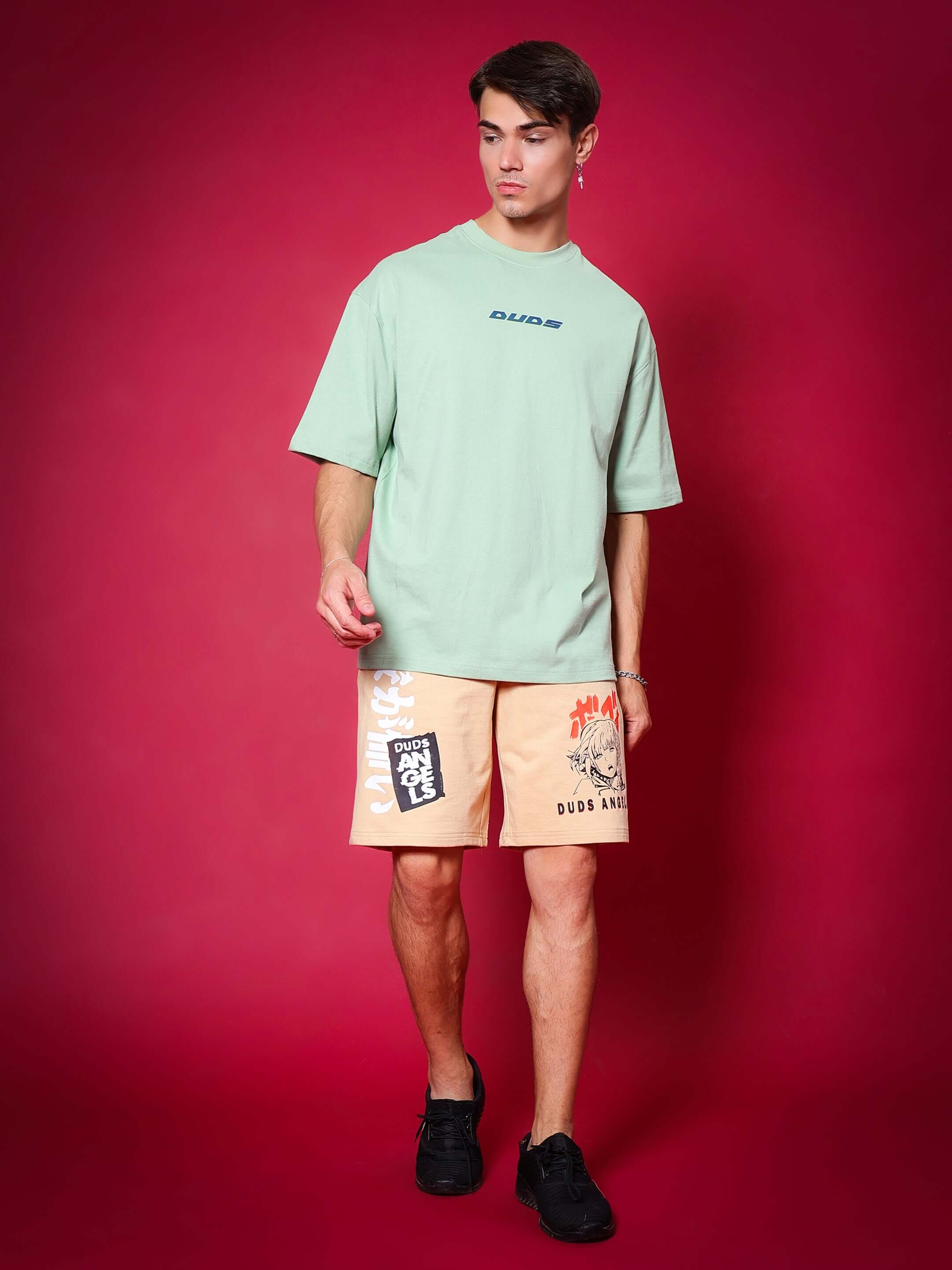 Model wearing DUDS Anime Girl regular fit shorts in light orange with graphic print, paired with a green oversized t-shirt and black sneakers.