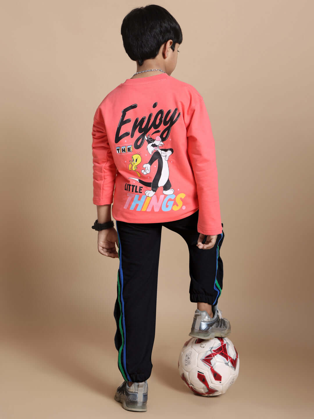 Child wearing black joggers with colorful stripes, paired with a pink shirt featuring playful graphics, standing with a soccer ball.