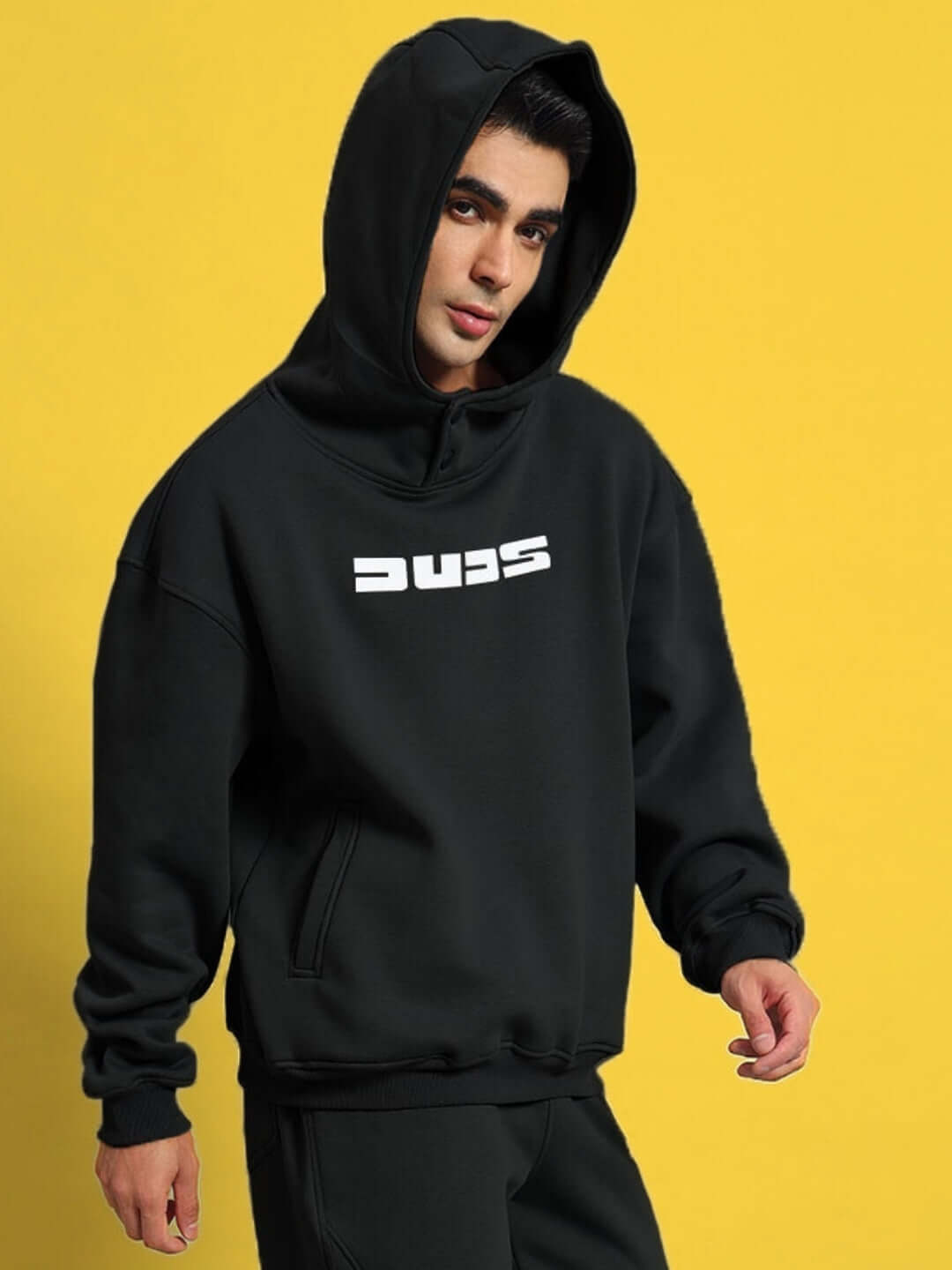 Model wearing WEARDUDS SHOOTER FLEECE CO-ORD BLACK hoodie in front of a yellow background, showcasing stylish design and comfort.