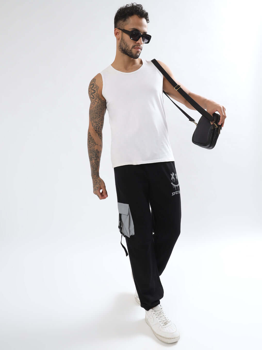 Man wearing black Smiley Reflector Cargo Jogger by DUDS paired with white tank top and sunglasses, showcasing casual street style fashion.