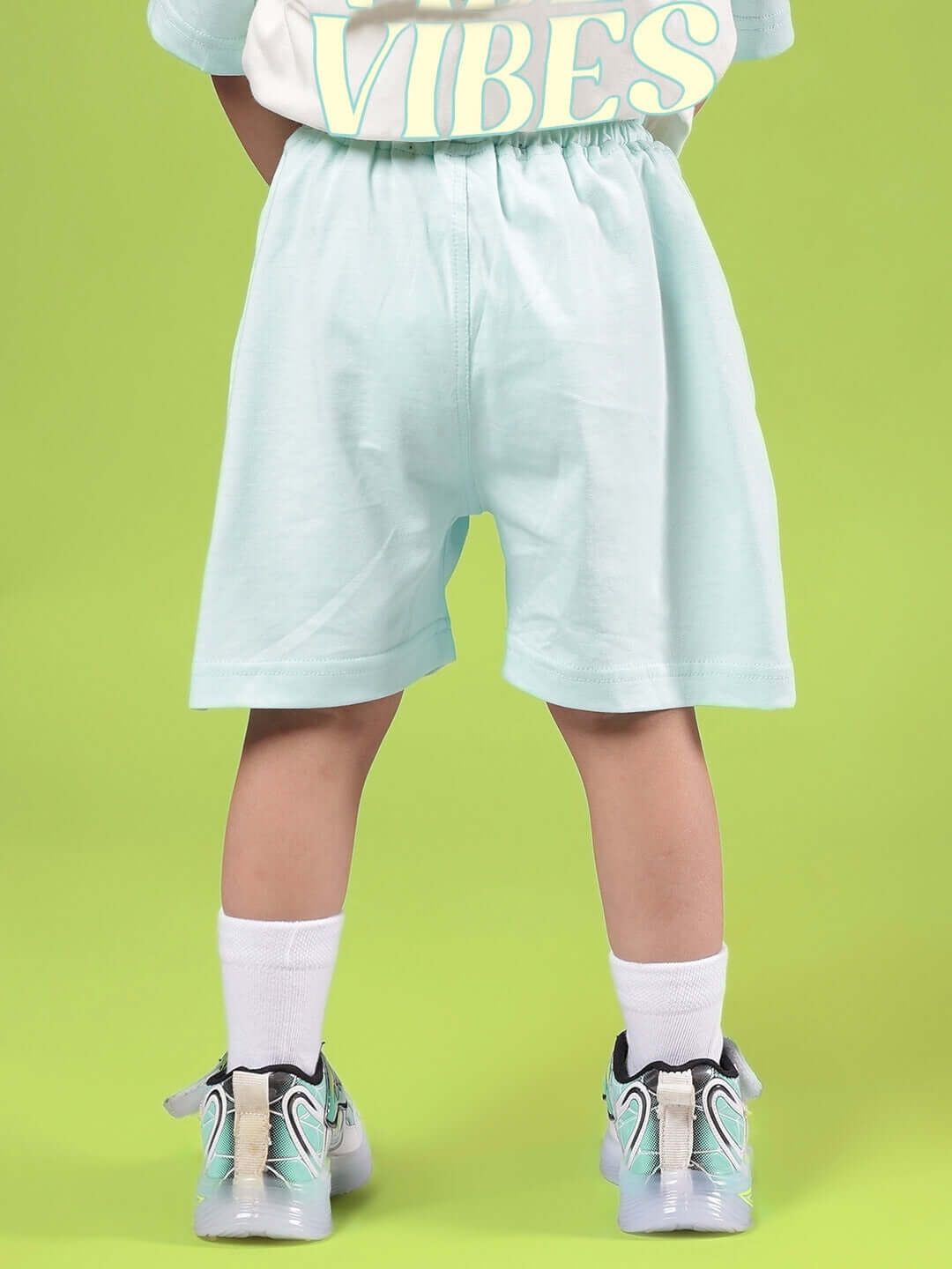 Child wearing DUDS VIBES SHORTS FOR BOYS & GIRLS SKY BLUE with sneakers on a green background