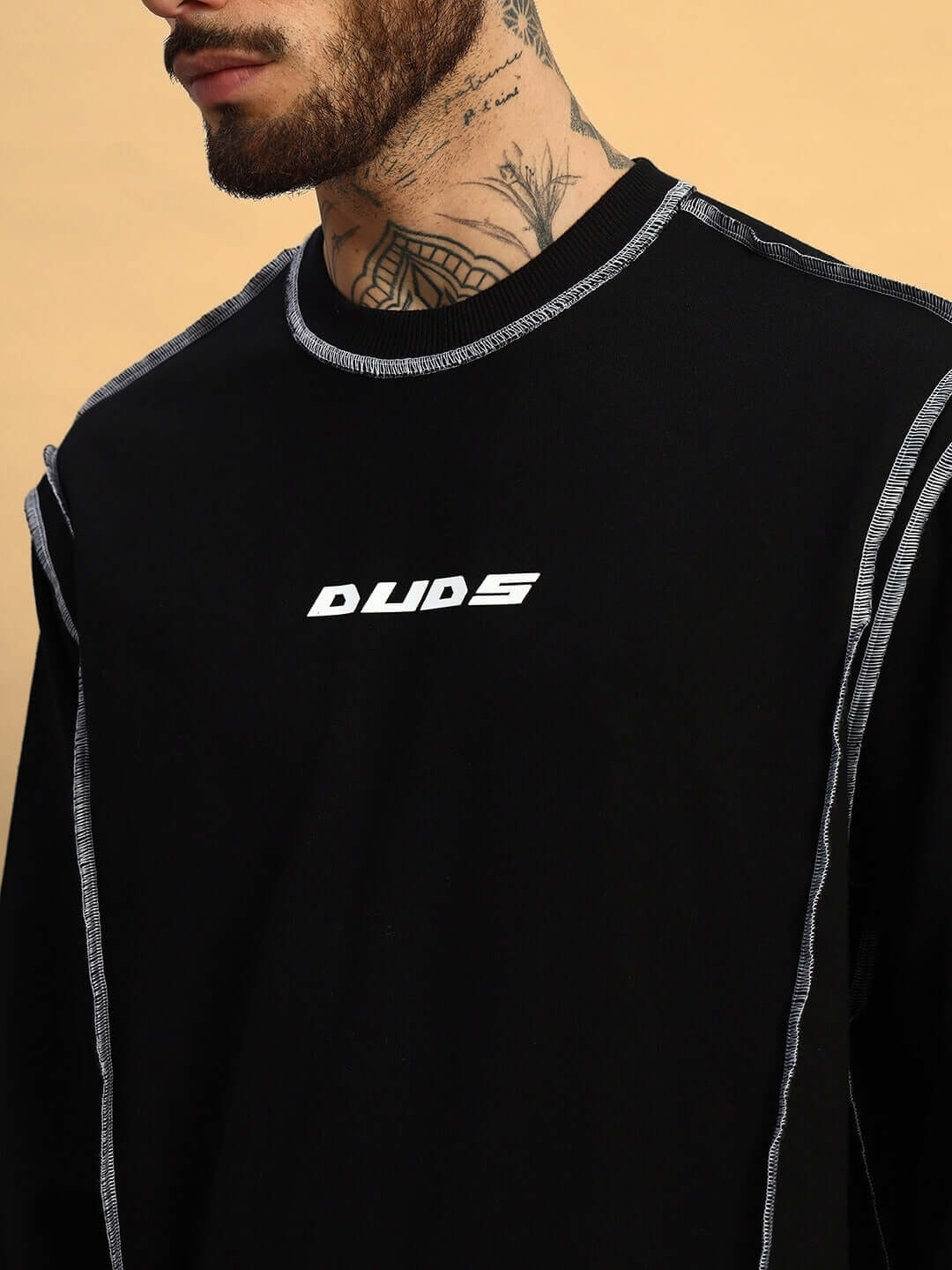 Dynamic oversized black sweatshirt made from premium cotton French terry with contrast stitching, worn by tattooed model. Ideal for casual wear.
