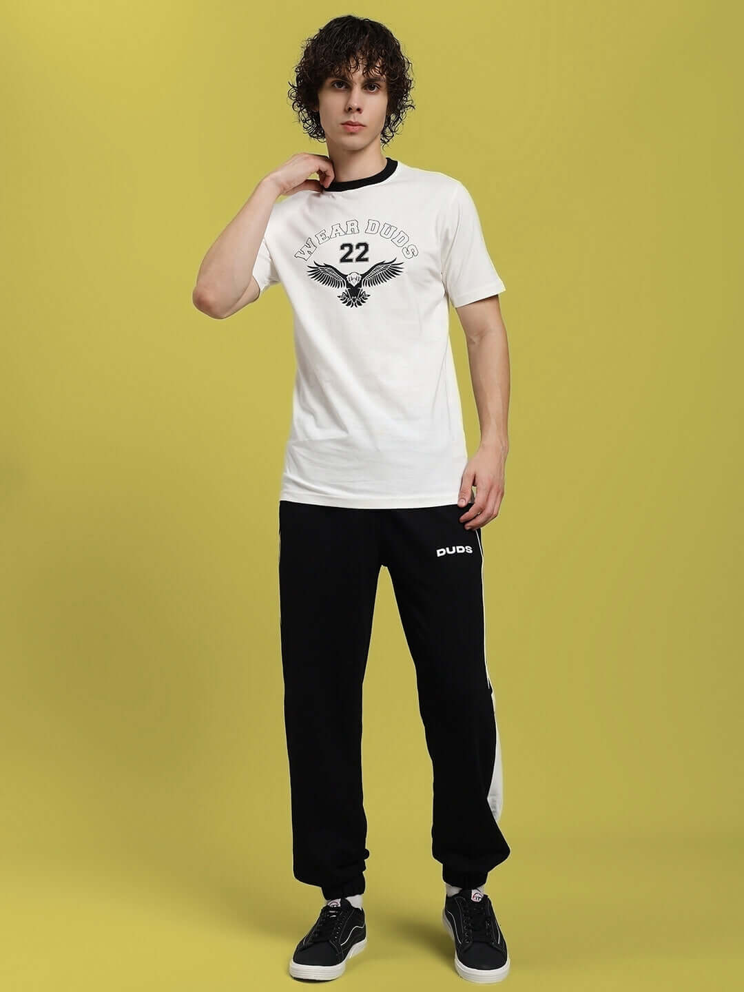 Model wearing Eagle Wings Regular Fit T-Shirt in White, made of premium 100% cotton, styled with black trousers, on a yellow background.
