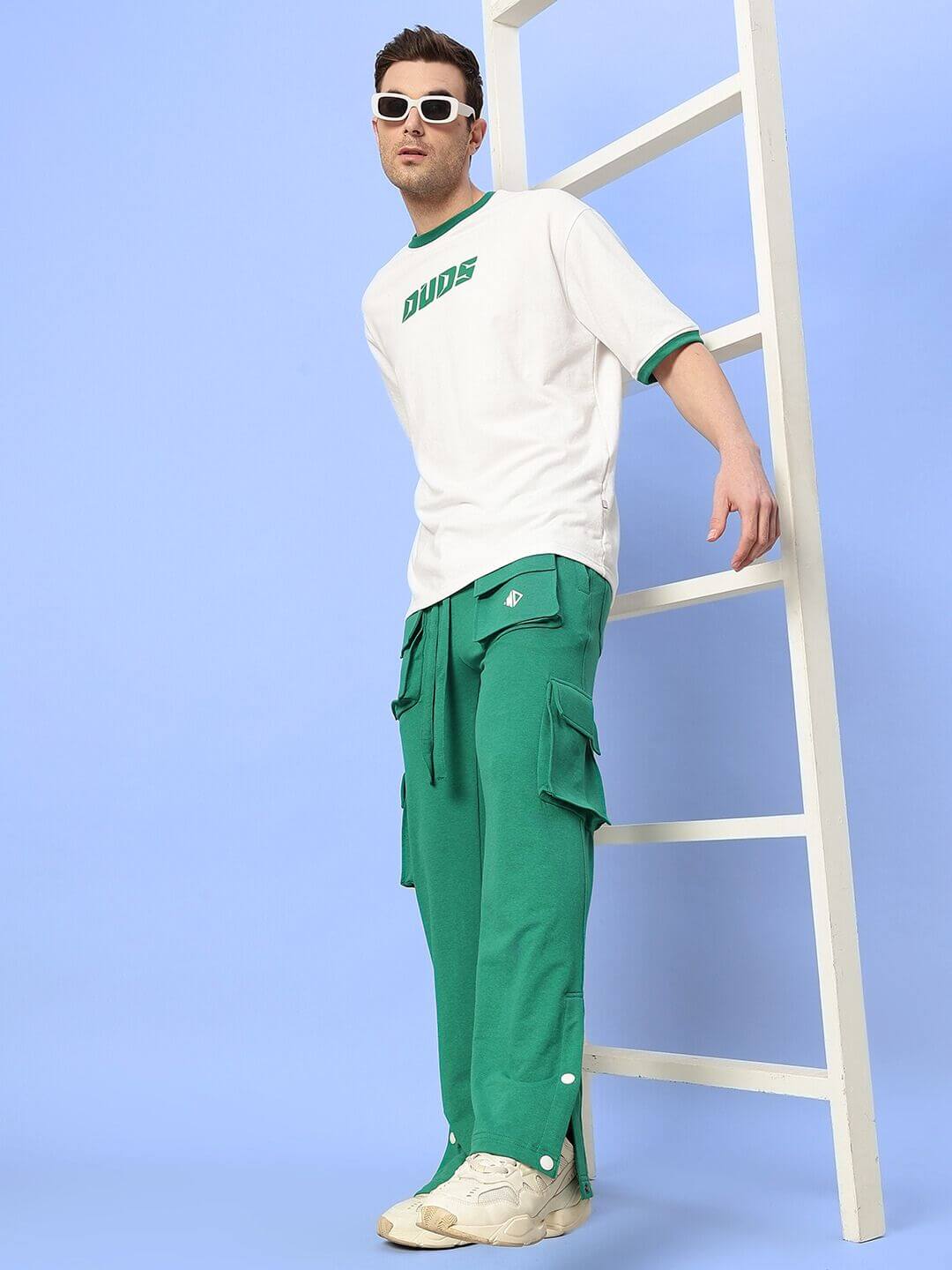 Model wearing Easton Boxy Fit T-Shirt White-Green with green pants standing against blue background.