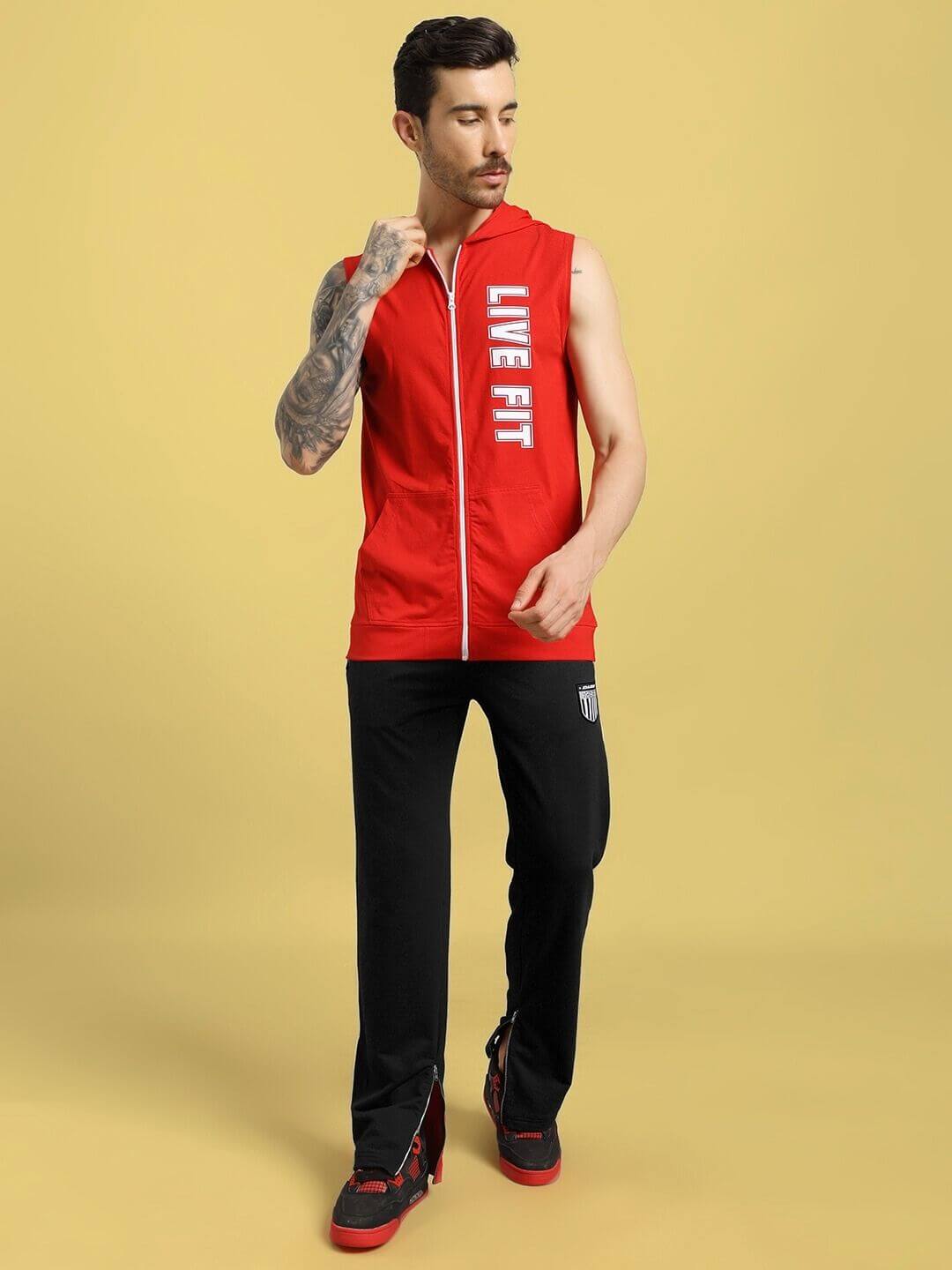 Man wearing ELEGANT RELAXED-FIT JOGGERS BLACK paired with red sleeveless hoodie against beige background