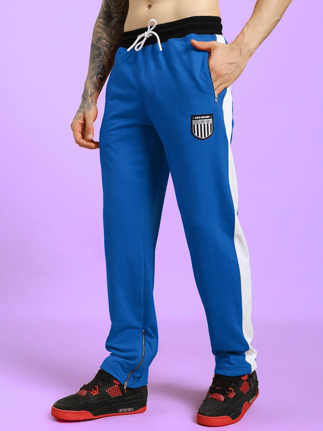 Man wearing ELEGANT RELAXED-FIT JOGGERS BLUE with side stripe, standing on a purple background, showcasing comfort and style.