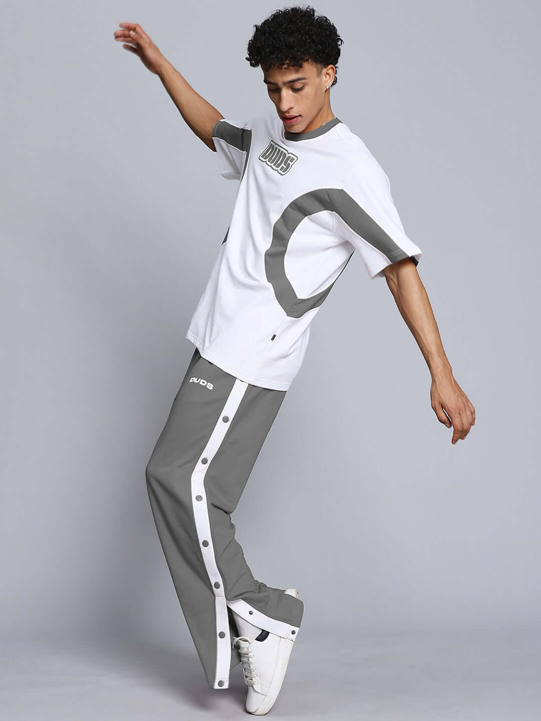 Model wearing EZEL grey relaxed fit jogger pants by DUDS, showcasing sporty style with side buttons, paired with matching t-shirt.