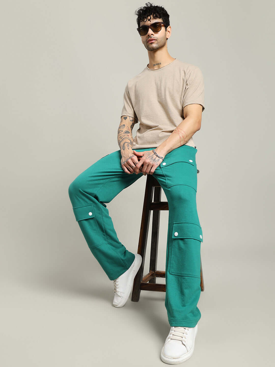 Man wearing ELEX REGULAR FIT T-SHIRT BEIGE with teal pants, seated on a stool, showcasing casual style and comfort.