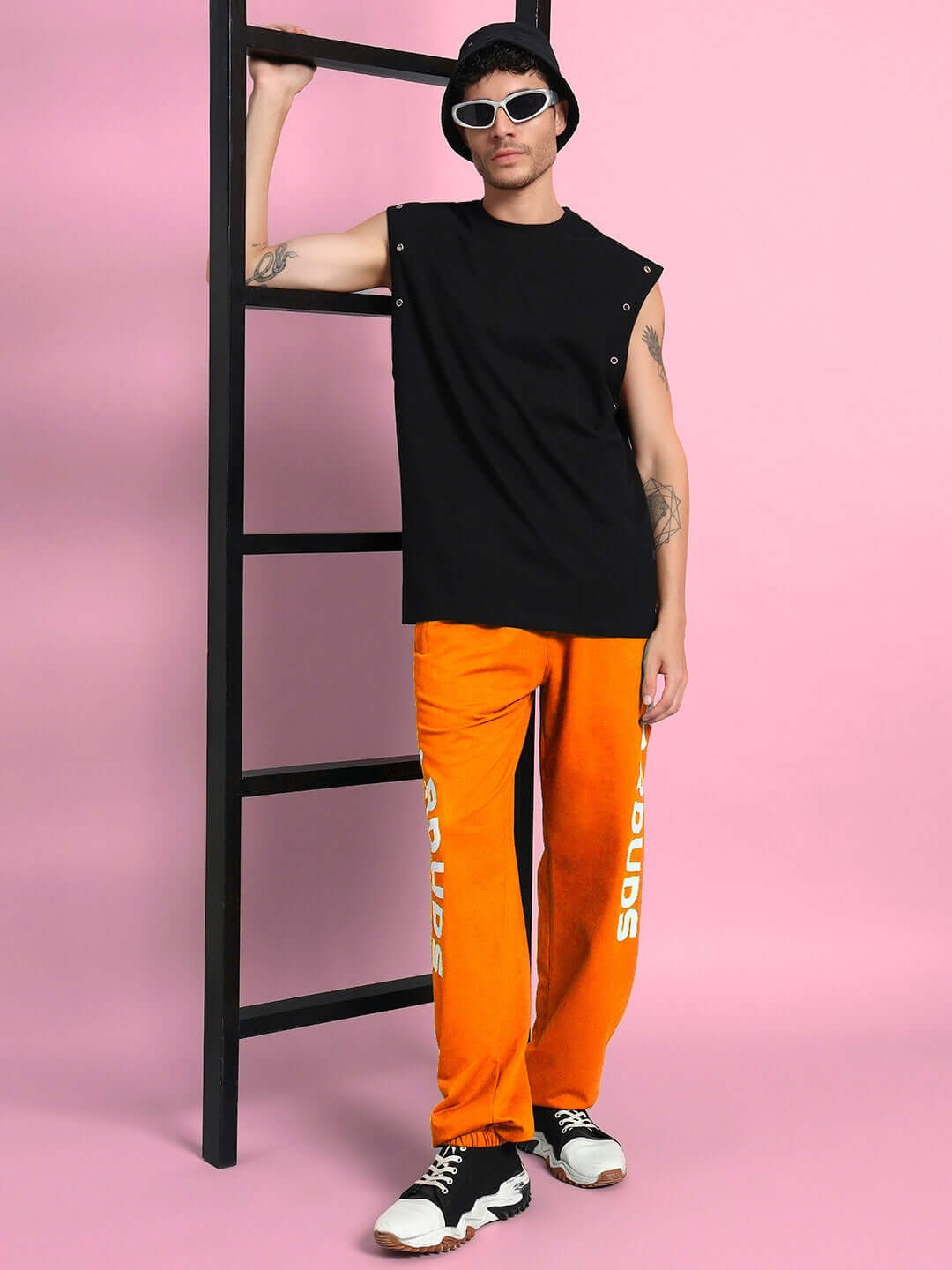 Model wearing ELLEN RELAXED FIT JOGGER ORANGE with black top and sneakers, showcasing streetwear style on a pink background.