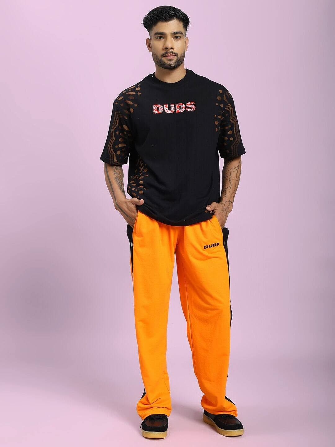 Model wearing EMBER BOLT SIDE JOGGER IN ORANGE with black shirt on pink background.