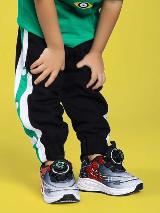 Child wearing EMIRATI JOGGER FOR BOYS AND GIRLS BLACK GREEN with colorful sports shoes on a yellow background.