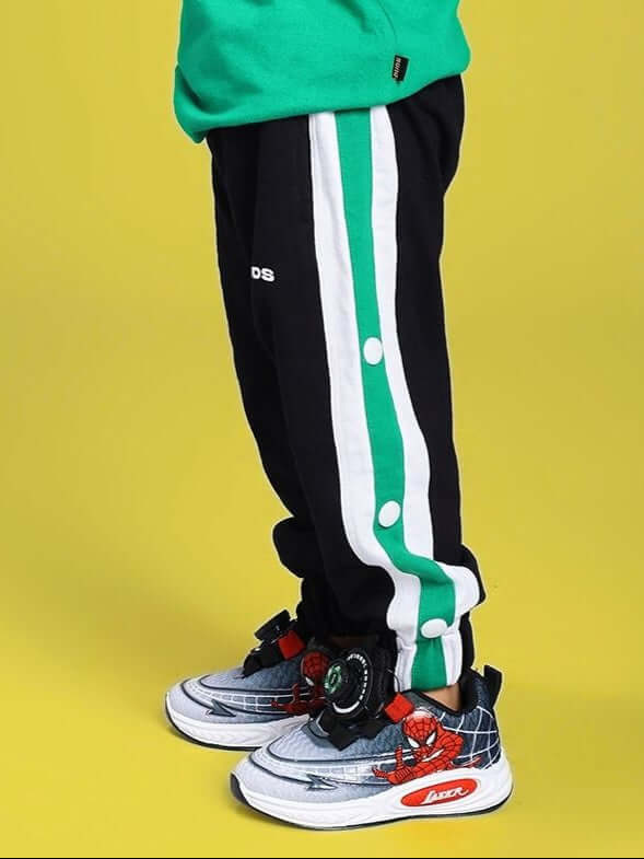 Child wearing EMIRATI JOGGER FOR BOYS AND GIRLS BLACK GREEN on yellow background with colorful sneakers.