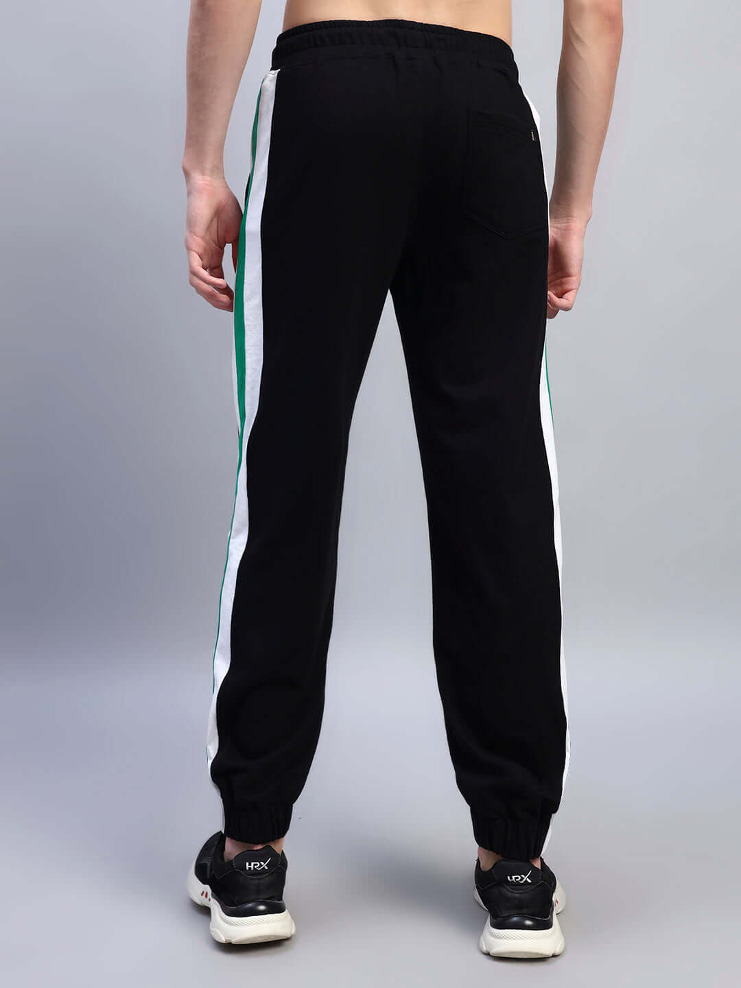 Rear view of EMIRATI STRIPES JOGGERS BLACK-GREEN with green side stripes, showing sporty design on a person wearing sneakers.