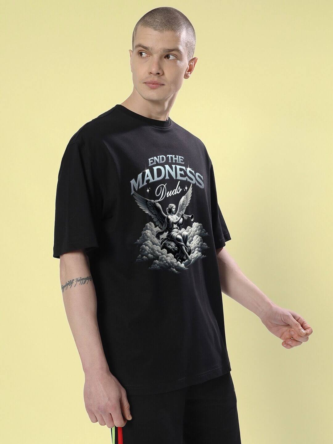 Model wearing END THE MADNESS OVER-SIZED T-SHIRT BLACK with bold graphic design, showcasing streetwear style and relaxed fit.