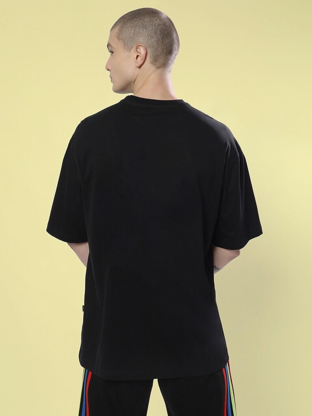 Back view of model wearing END THE MADNESS OVER-SIZED T-SHIRT BLACK, showcasing its relaxed fit and bold design.