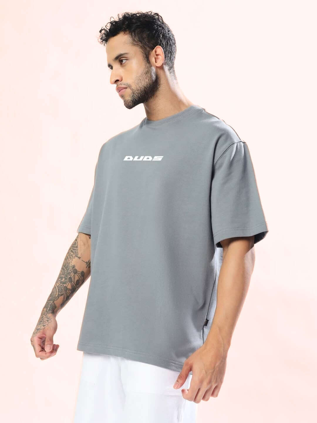 Man wearing grey oversized 'Enjoy the Wind' t-shirt by DUDS, offering a customizable fit and handmade quality.