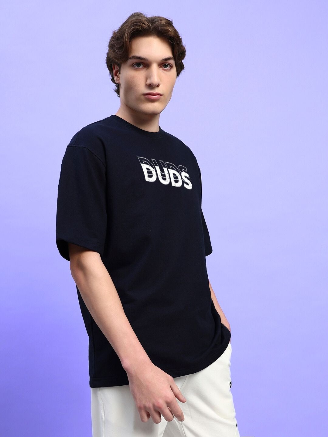 Model wearing EVERYTHING IS TEMPORARY OVER-SIZED T-SHIRT BLACK with lettering on chest, styled with white pants on a lavender background.