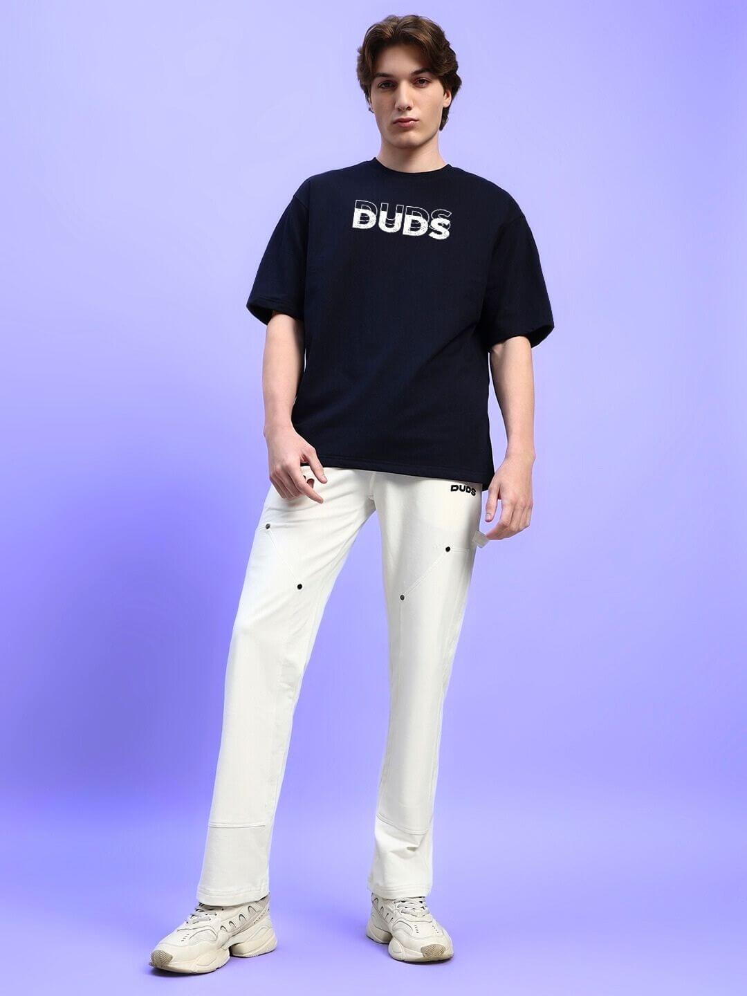 Model wearing black EVERYTHING IS TEMPORARY OVER-SIZED T-SHIRT BLACK with white pants, standing on purple background.