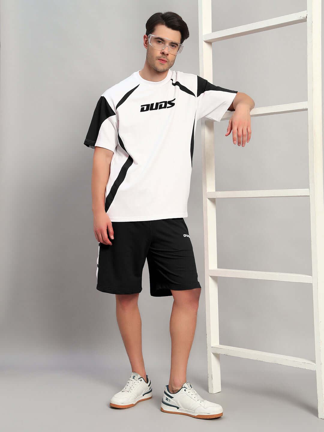 Man wearing Ezel Regular Fit Shorts Black Cotton, styled with a Duds shirt, showcasing modern streetwear look on model near ladder.