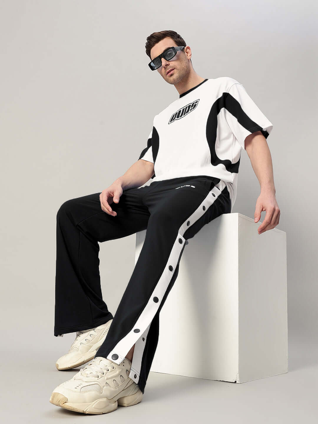 Model wearing EZEL RELAXED FIT CO-ORD SET WHITE-BLACK, showcasing stylish monochrome off-duty casual outfit, seated on minimalist block.