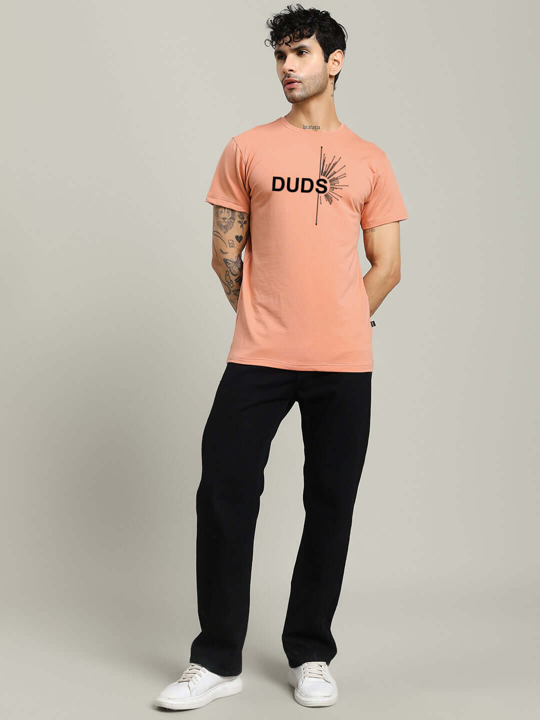 Model wearing peach Fallen Angle regular fit T-shirt in 100% cotton, styled with black pants; features 'DUDS' graphic design.