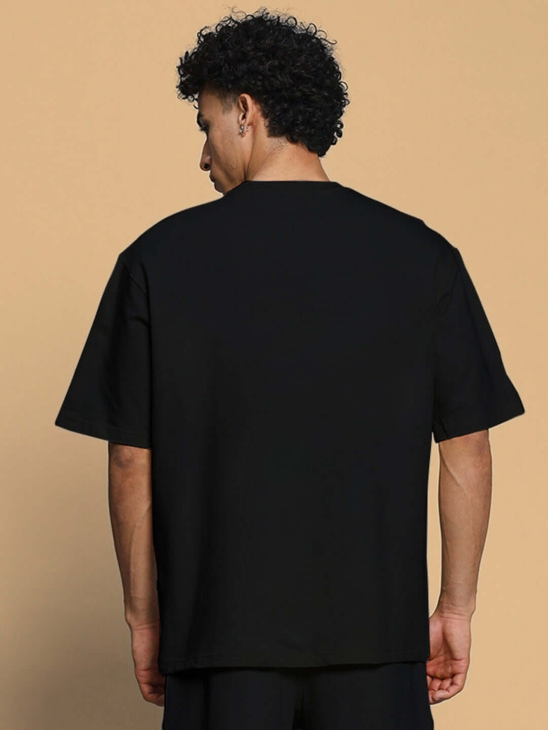 Back view of a man wearing a FANCY DREAM OVER-SIZED T-SHIRT BLACK, showcasing its relaxed fit and comfortable cotton fabric for casual style.