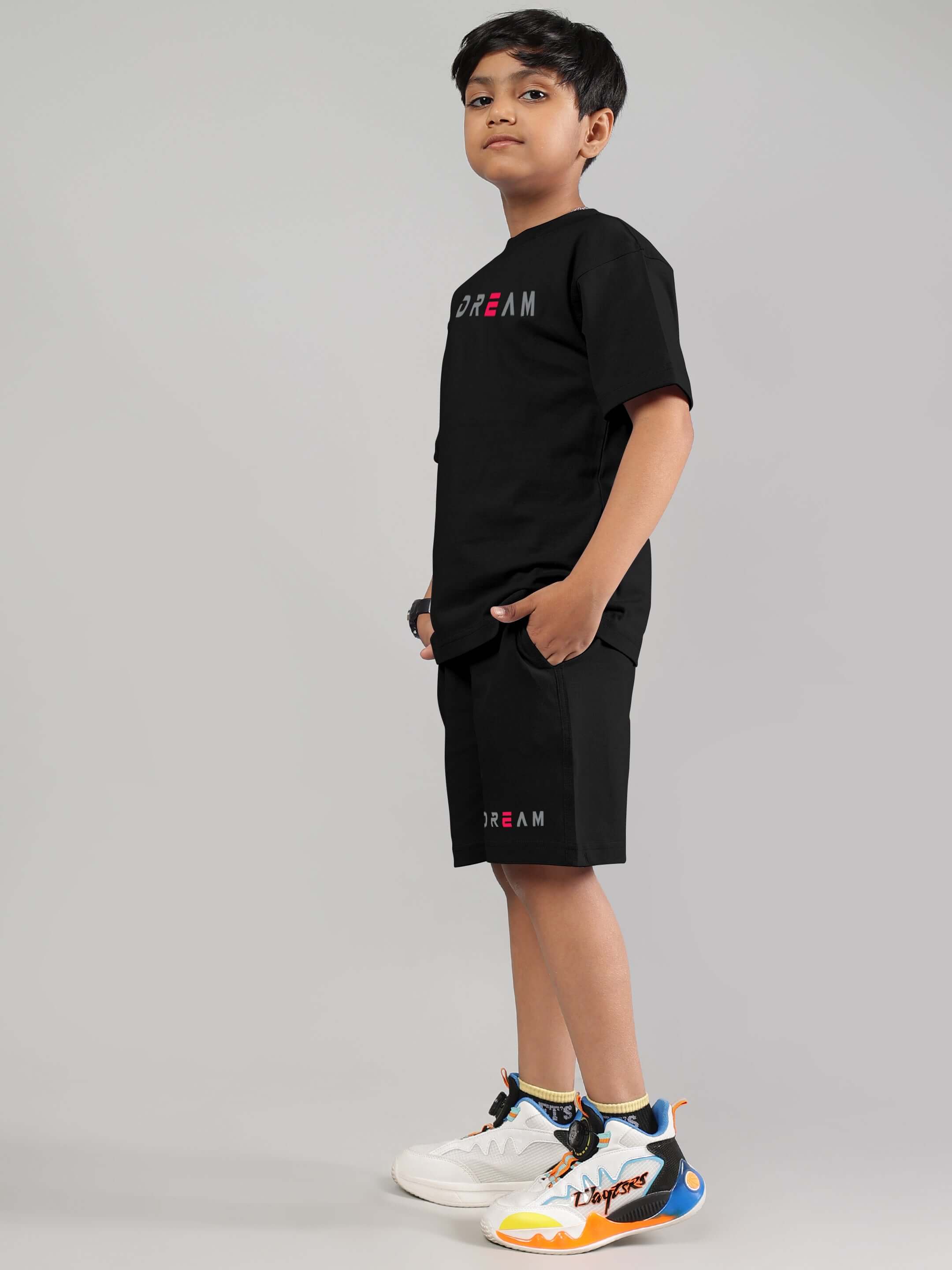 Boy wearing Fancy Dream black co-ord set from DUDS, featuring a T-shirt and shorts, styled with colorful sneakers. Ideal for boys and girls.