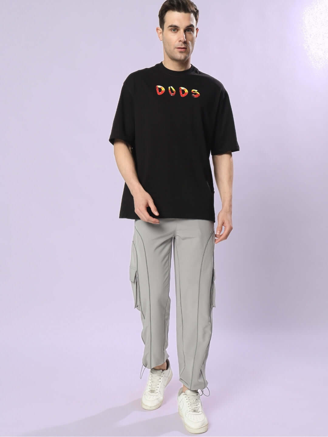 Model wearing Fantasy Mushroom Oversized T-Shirt in black with "DUDS" logo, paired with gray cargo pants and white sneakers.