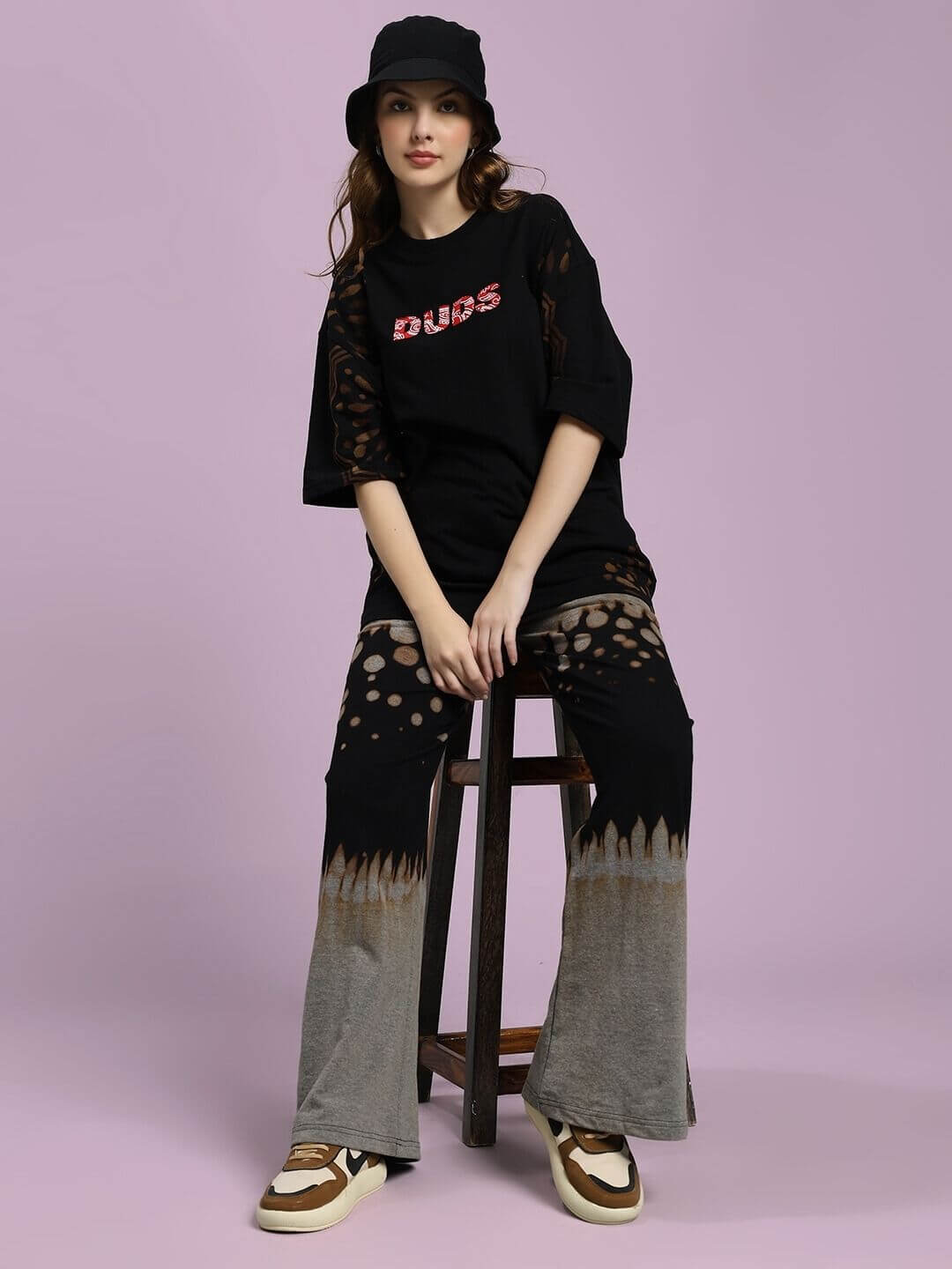 Model wearing WOMEN'S SHADOW SWIRL TIE-DYE T-SHIRT BLACK sitting on a stool with casual outfit and accessories