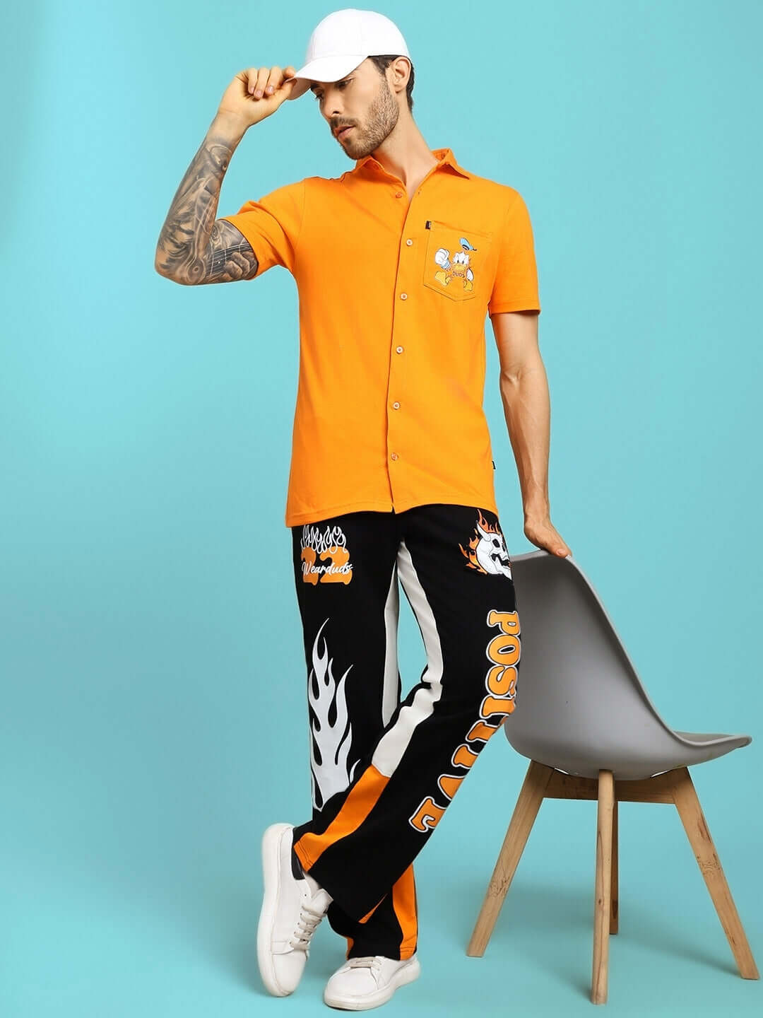 Model wearing FEARLESS CONTRAST POSITIVE RELAXED FIT JOGGERS BLACK-ORANGE with orange shirt, posing against a blue background.