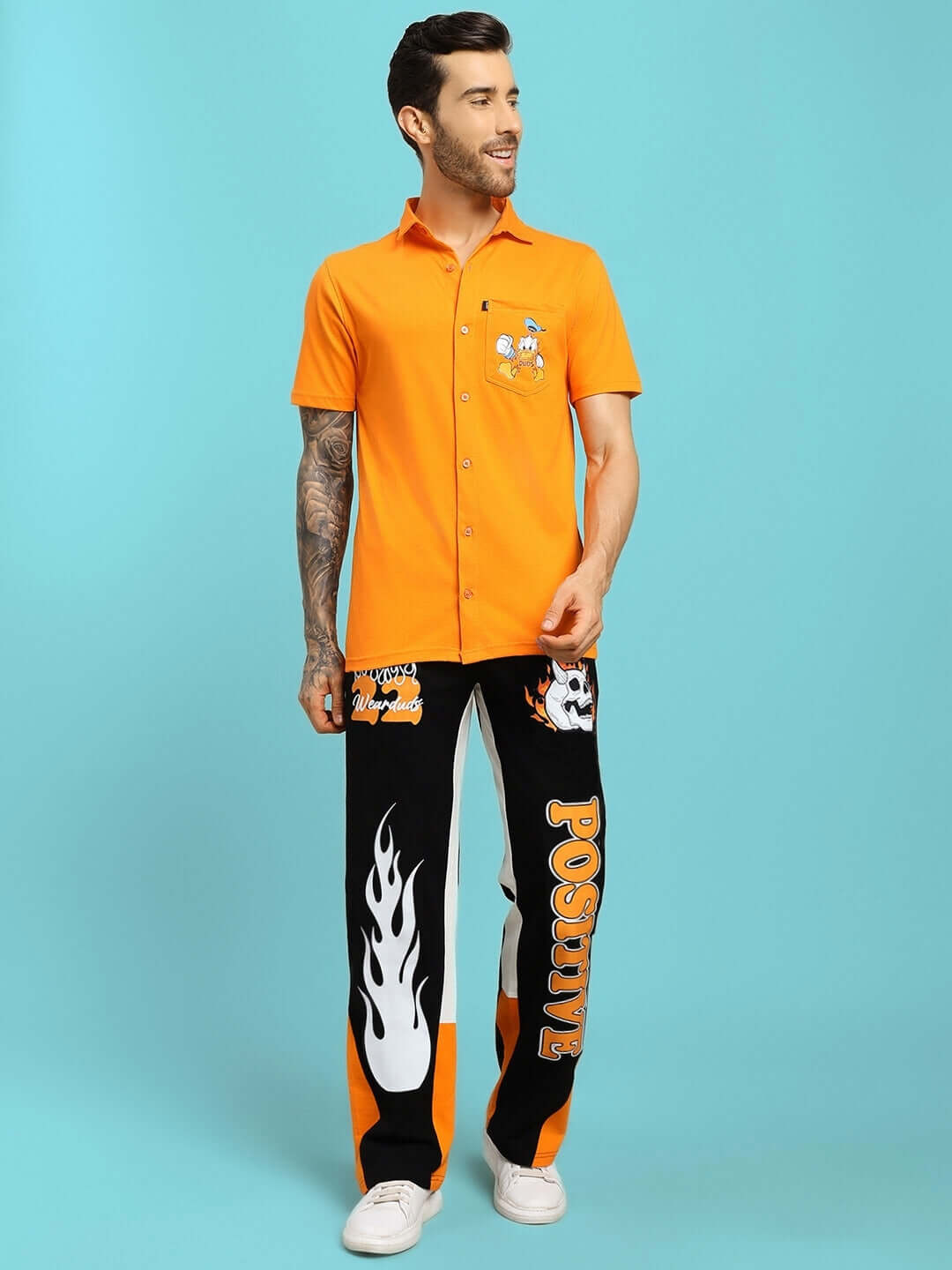 Man wearing FEARLESS CONTRAST POSITIVE RELAXED FIT JOGGERS BLACK-ORANGE with orange graphic shirt and white sneakers.