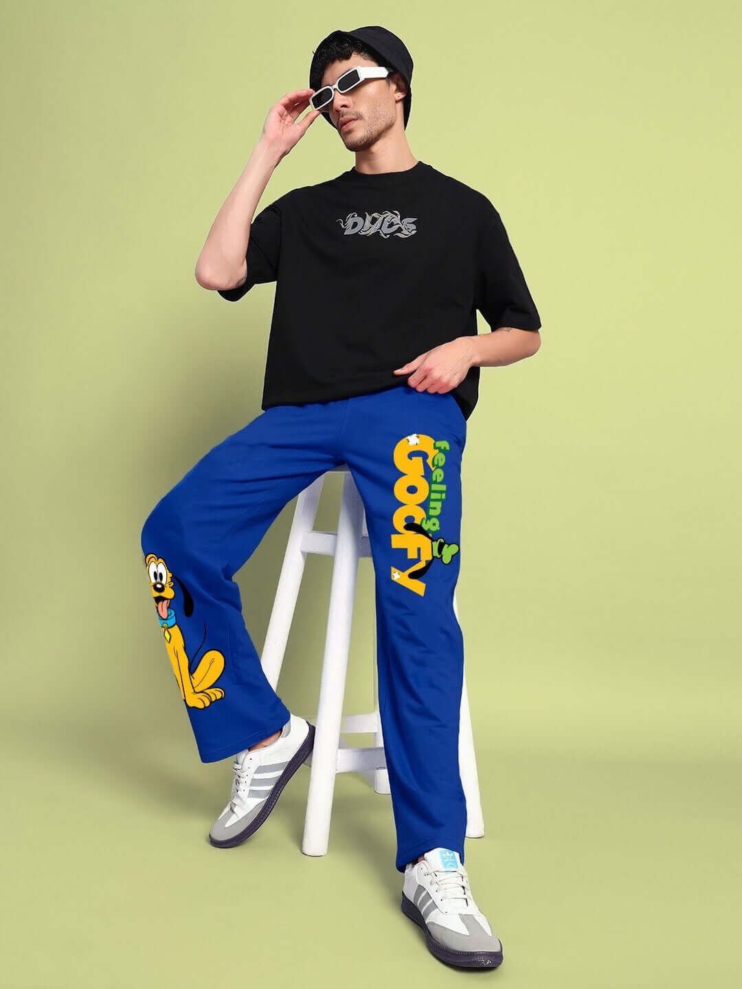 Model wearing FEELING GOOFY RELAXED FIT JOGGER BLUE with a playful design, seated on a stool in a casual pose.