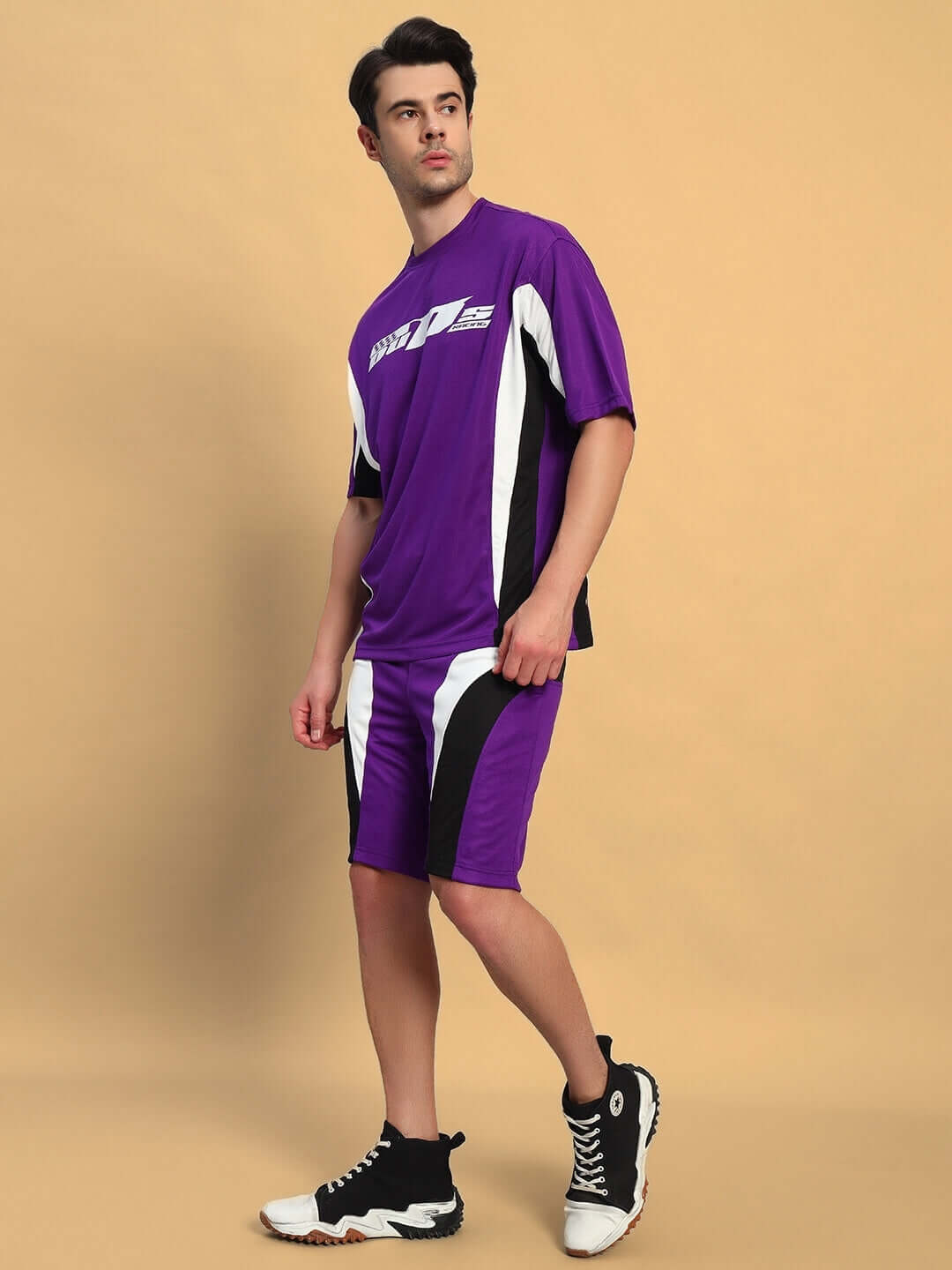 Person wearing FIFA COLORBLOCK CO-ORD SET PURPLE, featuring a purple t-shirt and shorts, standing against a beige background.