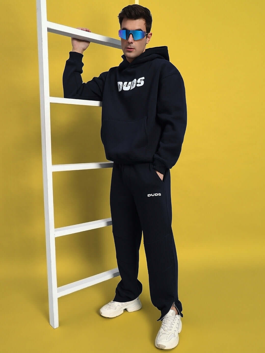 Model wearing FIGHT NIGHT FLEECE CO-ORD NAVY BLUE set with sunglasses, posing against yellow background