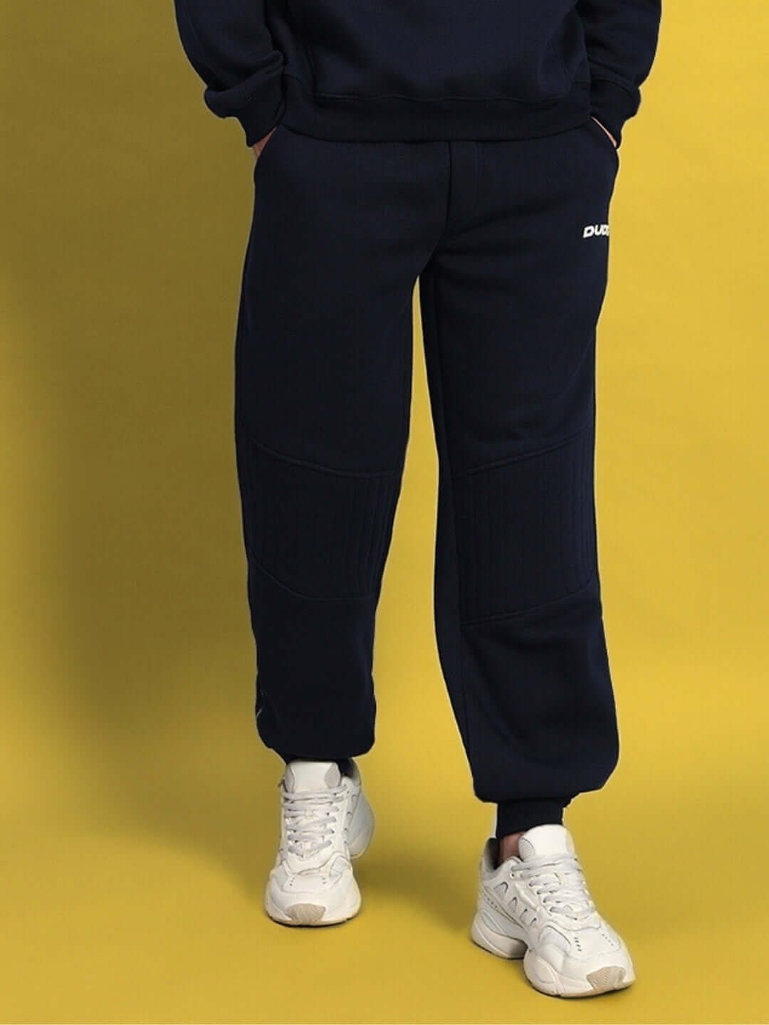 Navy blue fleece jogger pants for Fight Night, featuring a stylish and comfortable design, paired with white sneakers on a yellow background.