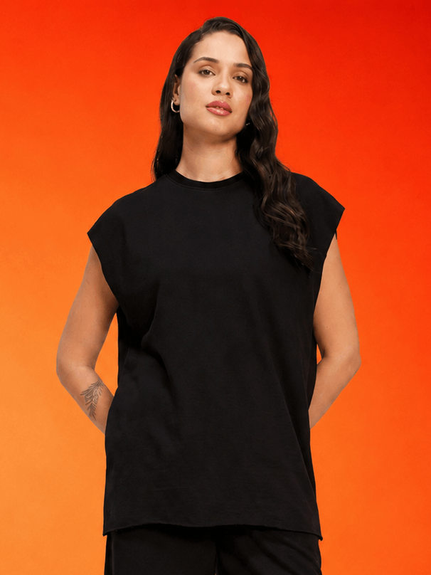WOMEN DRIVE MONOCHROME SLEEVELESS T-SHIRT BLACK on a model against an orange background, showcasing sporty-chic style.