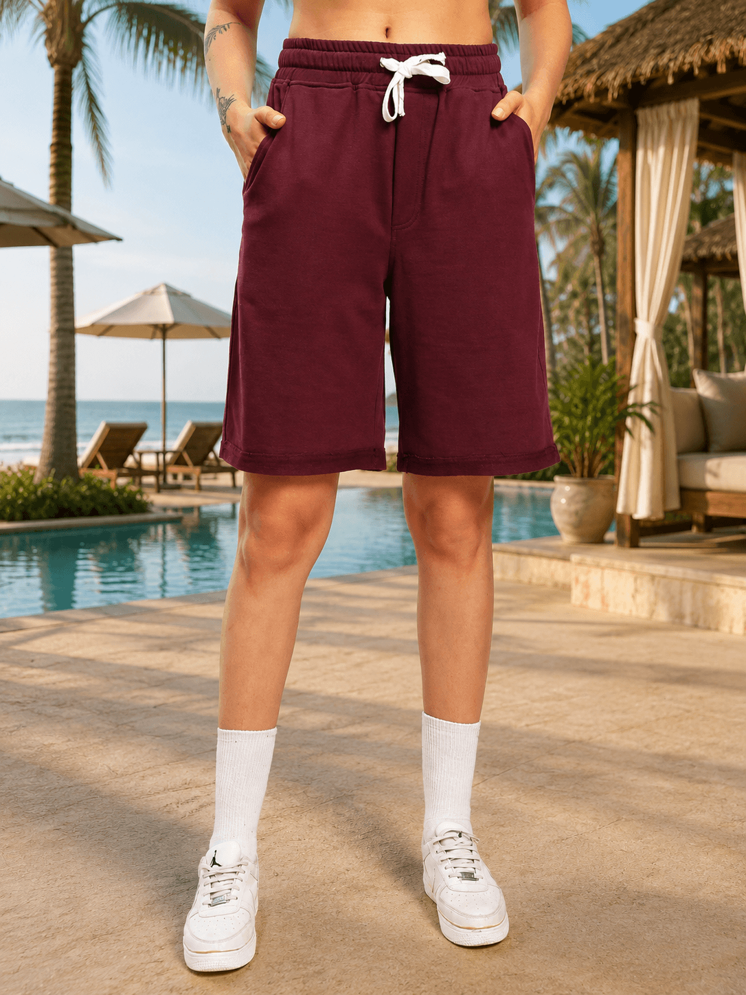 Women Drive Monochrome Relaxed Fit Shorts Maroon worn with white sneakers by the poolside, showcasing a stylish summer look.