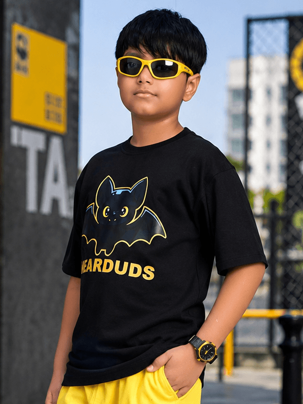 Midnight Bat T-Shirt for Boys Girls Black worn by a boy with sunglasses and yellow shorts outdoors.