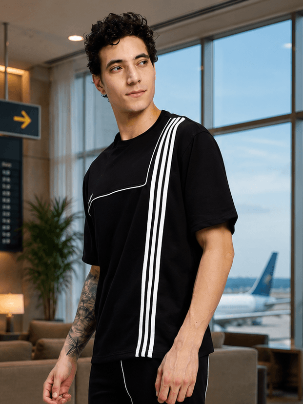 Youth Contrest Piping T-Shirt Black displayed on a model in an airport setting, featuring bold white piping.