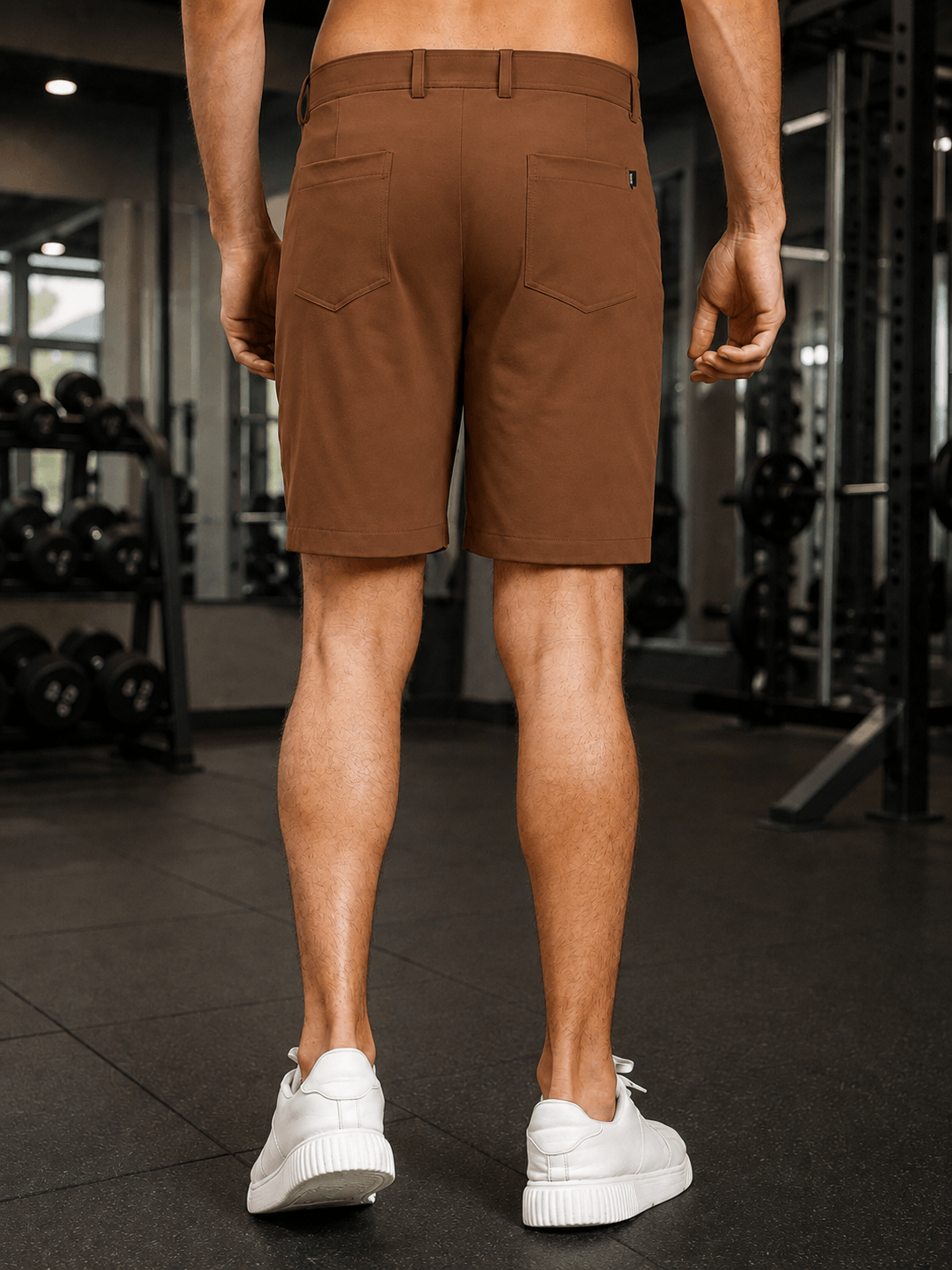 PRIME FIT PERFORMANCE REGULAR SHORTS DARK BROWN shown from the back in a gym setting, paired with white sneakers.