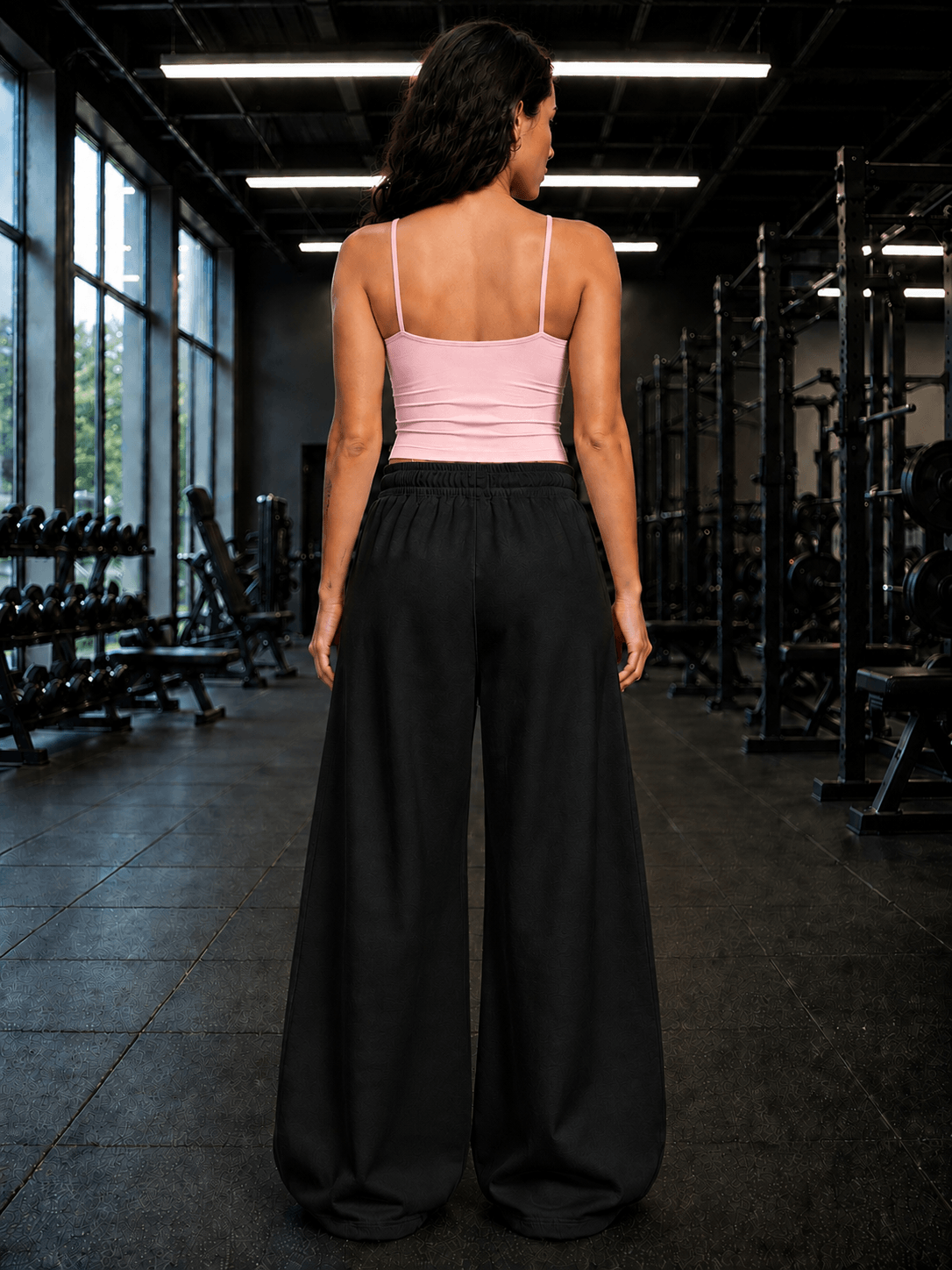 Woman wearing WOMEN SEAMLESS COTTON CROP-TOP PINK and black wide-leg pants in a gym setting.