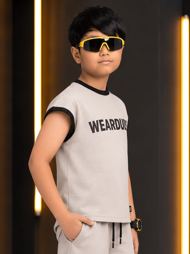 MONO EDGE SLEEVELESS T-SHIRT FOR BOYS GIRLS BEIGE worn by a boy with stylish sunglasses in a modern setting.