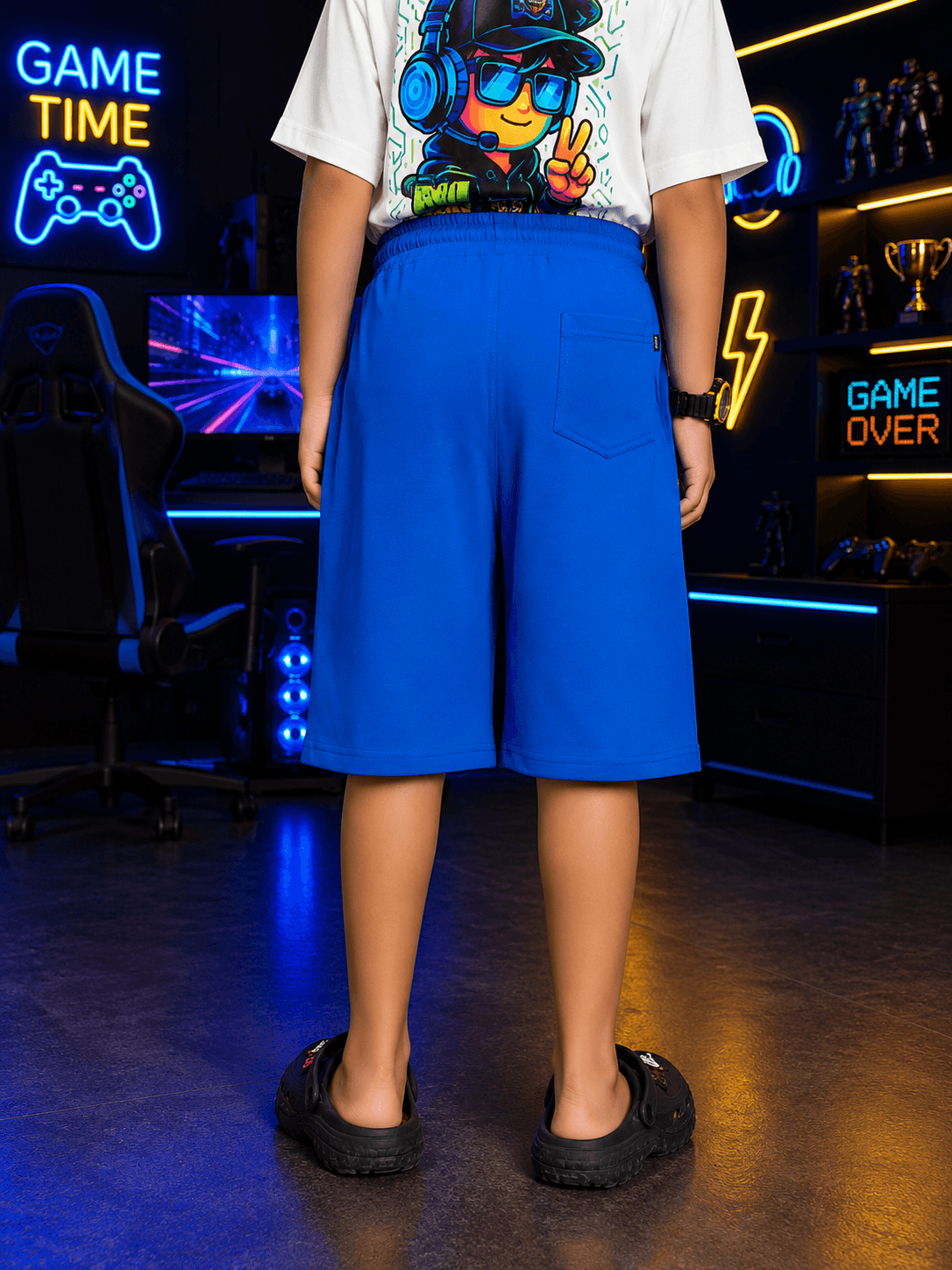 FUSION SHORTS FOR BOYS GIRLS BLUE worn by a child from the back in a gaming room setting.