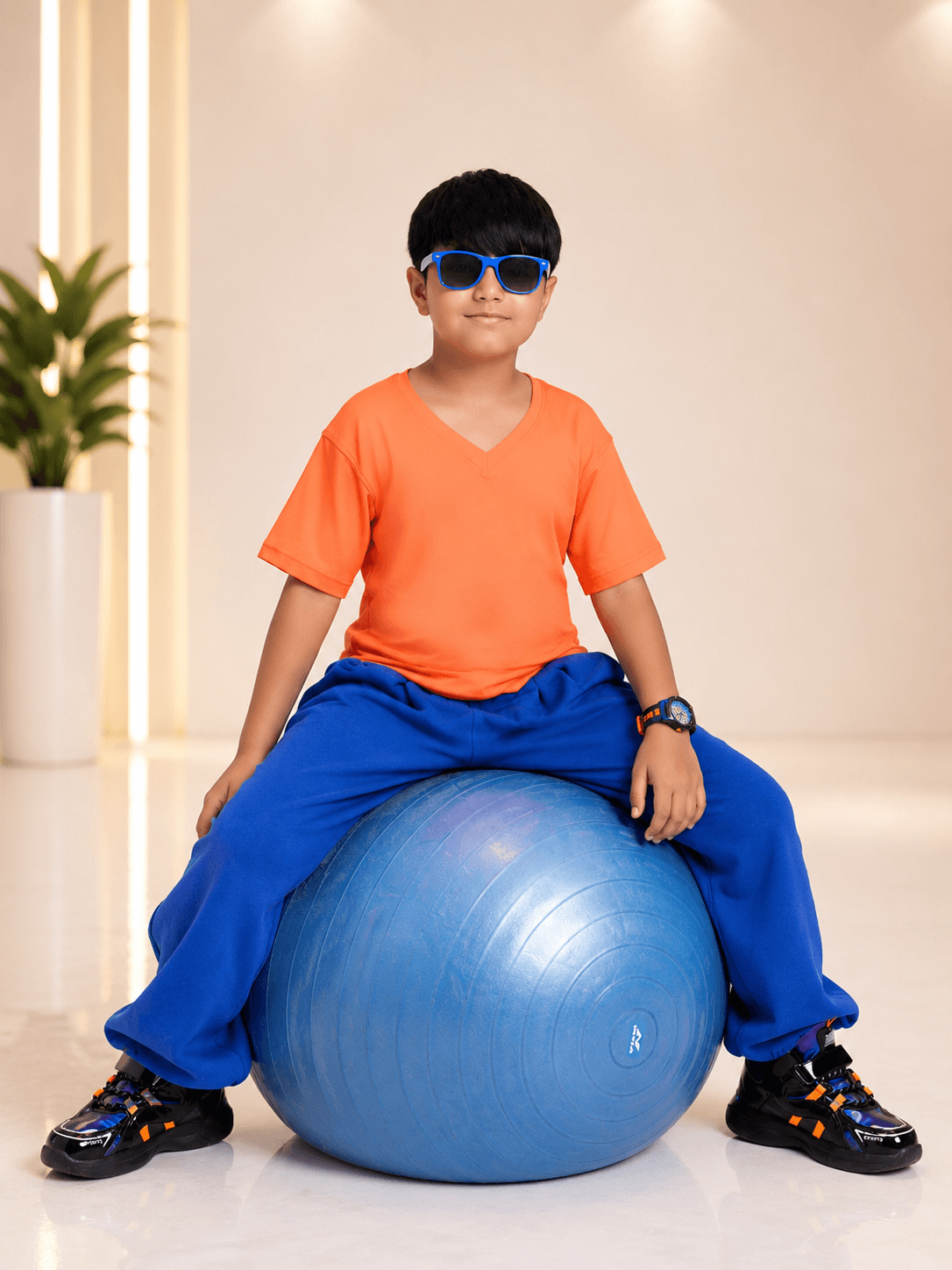 COOLFIT CO-ORD FOR BOYS GIRLS ORANGE BLUE outfit on a boy sitting on a blue exercise ball with sunglasses.